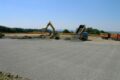 A construction site covered with gravel where an excavator is working and a truck is unloading gravel - FAUDI history